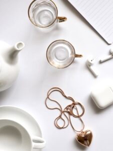 Minimalist flat lay featuring gold jewelry, glass cups, and a white tea set, perfect for luxury lifestyle themes.